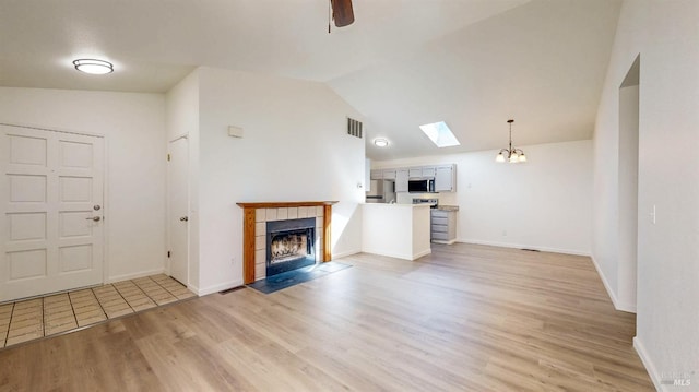 unfurnished living room featuring vaulted ceiling with skylight, light wood-type flooring, visible vents, a tile fireplace, and baseboards