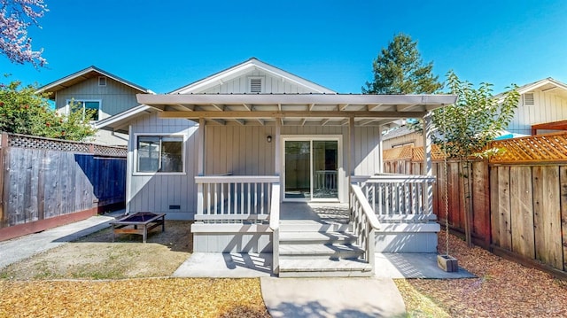 view of front of house with board and batten siding, an outdoor fire pit, a fenced backyard, and crawl space