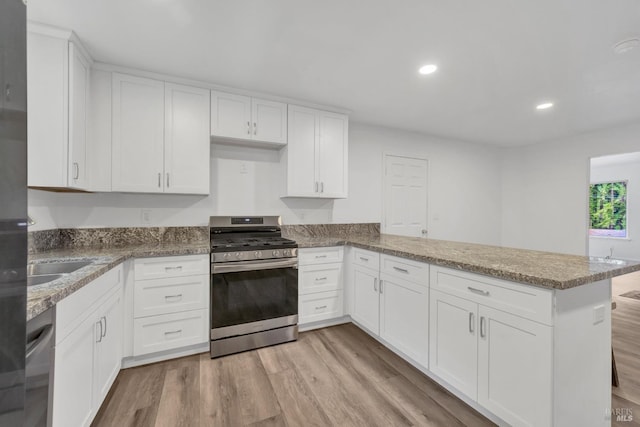 kitchen featuring light wood finished floors, light stone counters, stainless steel range with gas cooktop, a peninsula, and white cabinetry