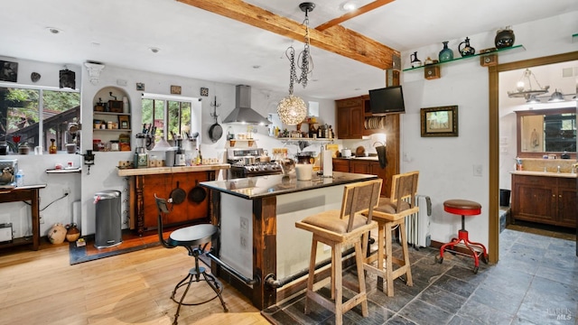 kitchen with range, wall chimney range hood, a center island, beamed ceiling, and pendant lighting