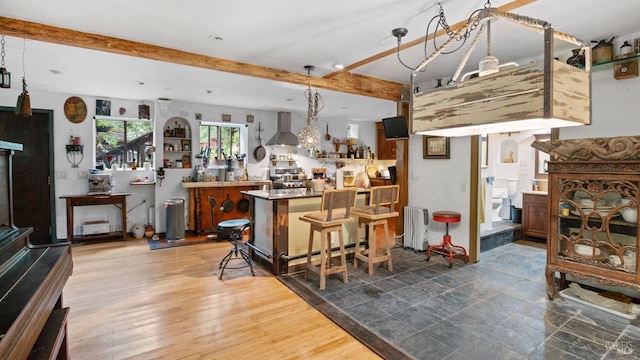 interior space with wall chimney range hood, a dry bar, radiator, and beamed ceiling
