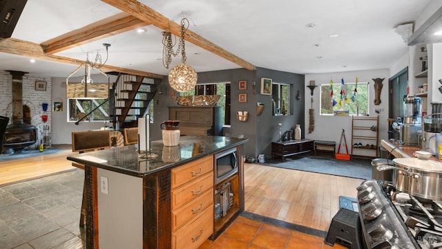kitchen featuring a wood stove, dark stone countertops, stainless steel microwave, open floor plan, and beam ceiling