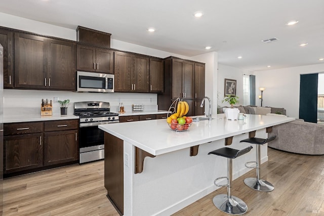 kitchen with a kitchen breakfast bar, stainless steel appliances, open floor plan, recessed lighting, and light wood-type flooring