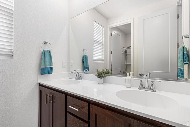 full bathroom featuring double vanity, a textured wall, and a sink