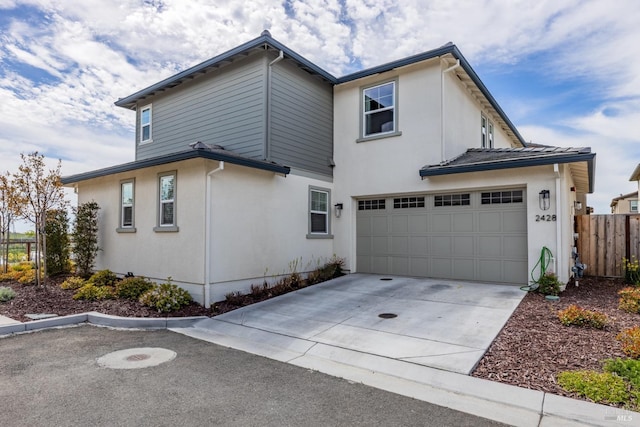 view of side of property featuring stucco siding, a garage, fence, and driveway