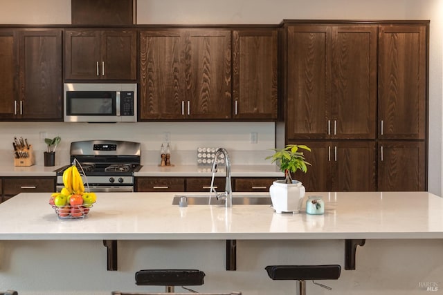 kitchen with dark brown cabinetry, a kitchen breakfast bar, a center island with sink, a sink, and stainless steel appliances