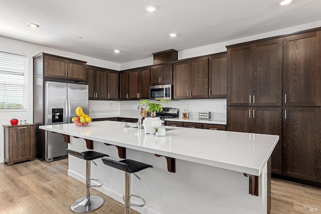 kitchen featuring a kitchen breakfast bar, dark brown cabinets, light countertops, stainless steel appliances, and light wood-style flooring