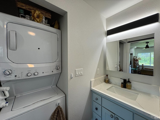 laundry area with a sink, ceiling fan, stacked washer and clothes dryer, and a textured wall