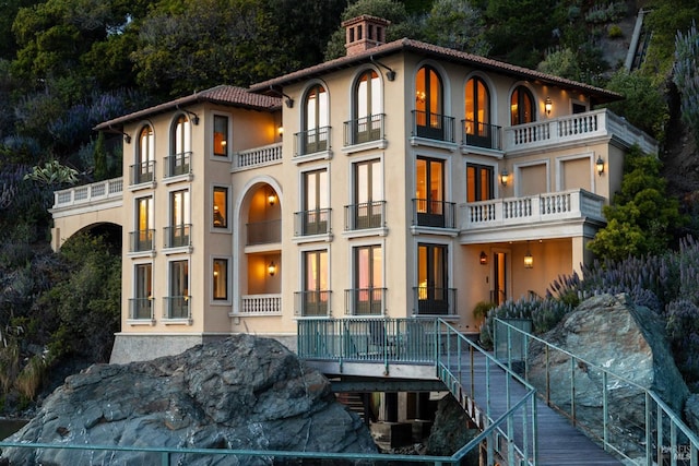 back of house featuring a tiled roof, a balcony, and stucco siding