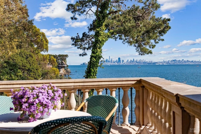 balcony with outdoor dining area, a water view, and a view of city