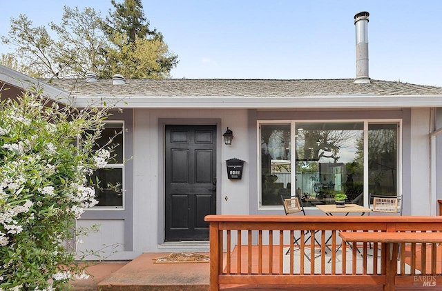 view of exterior entry with roof with shingles