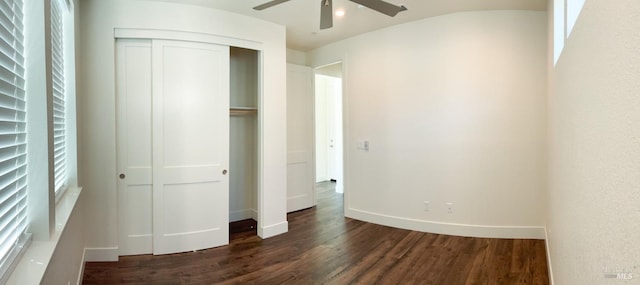 unfurnished bedroom with dark wood-style floors, a closet, baseboards, and ceiling fan