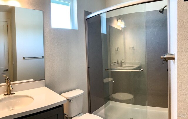 bathroom featuring toilet, a textured wall, a shower stall, and vanity