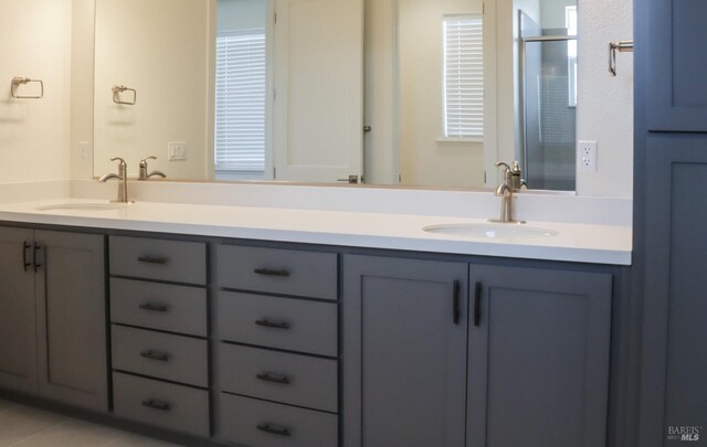 bathroom with a stall shower, double vanity, and a sink