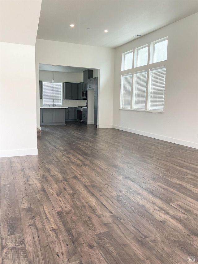 unfurnished living room with dark wood-style flooring, baseboards, recessed lighting, and a sink