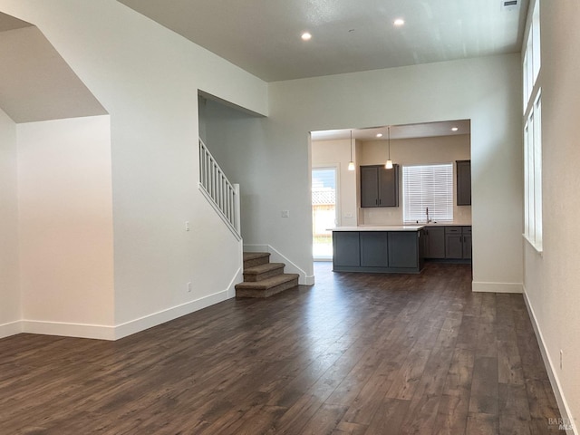 unfurnished living room with a sink, baseboards, dark wood-style floors, and stairs