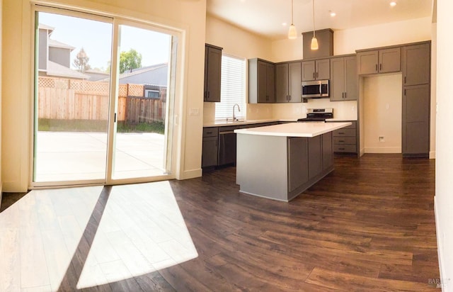 kitchen with a sink, light countertops, stainless steel appliances, dark wood-type flooring, and a kitchen island