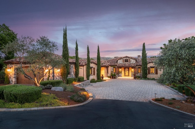 mediterranean / spanish house with curved driveway, stucco siding, and a tile roof