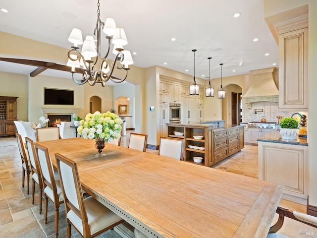 dining space featuring a lit fireplace, a chandelier, recessed lighting, stone tile flooring, and arched walkways