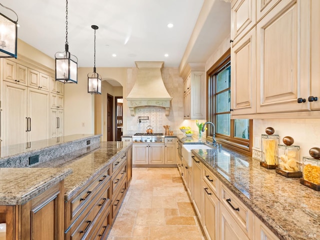 kitchen with a sink, premium range hood, stainless steel gas stovetop, decorative backsplash, and light stone counters