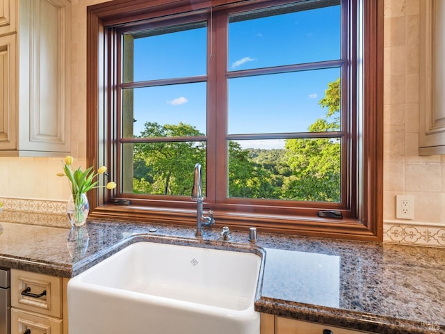 interior details featuring dark stone countertops, cream cabinets, a sink, and backsplash