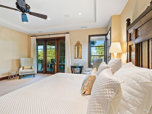 carpeted bedroom with a tray ceiling, access to exterior, ceiling fan, and multiple windows