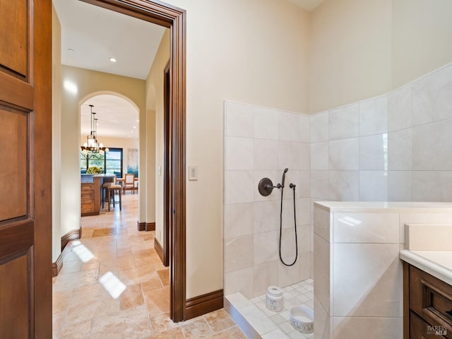 bathroom featuring vanity, baseboards, an inviting chandelier, a walk in shower, and stone tile floors