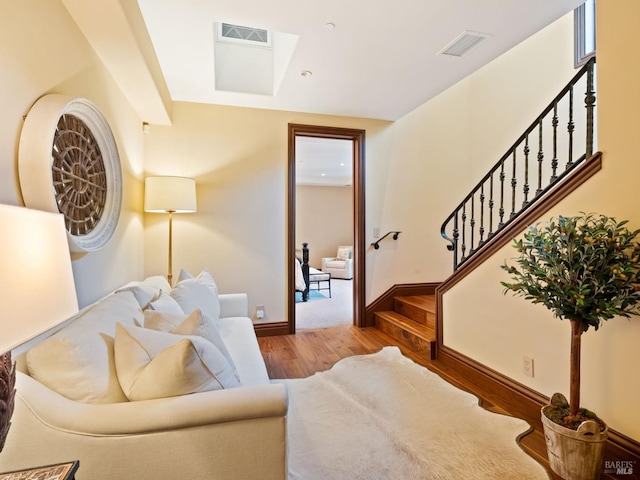 living area with wood finished floors, baseboards, visible vents, and stairs