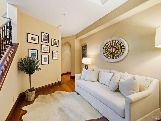 living area featuring arched walkways, baseboards, and wood finished floors