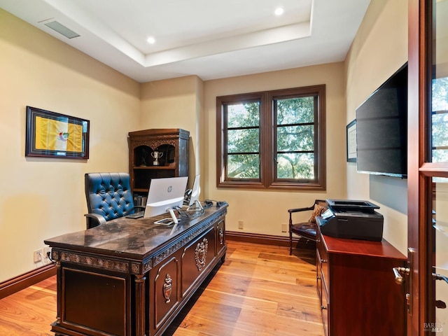 office space with light wood-style flooring, baseboards, visible vents, and a raised ceiling