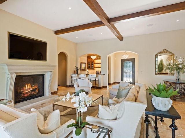 living area featuring a glass covered fireplace, arched walkways, beam ceiling, and recessed lighting