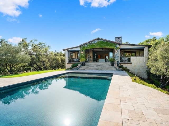 back of property featuring an outdoor pool, a chimney, and a patio area
