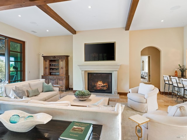 living room featuring beam ceiling, recessed lighting, arched walkways, and a glass covered fireplace