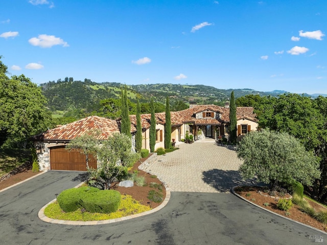 mediterranean / spanish home with a garage, aphalt driveway, a tiled roof, and a mountain view