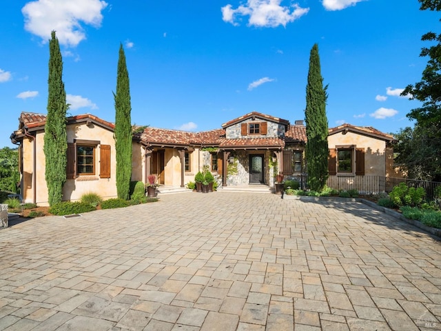 mediterranean / spanish house featuring fence, stucco siding, decorative driveway, and a tile roof