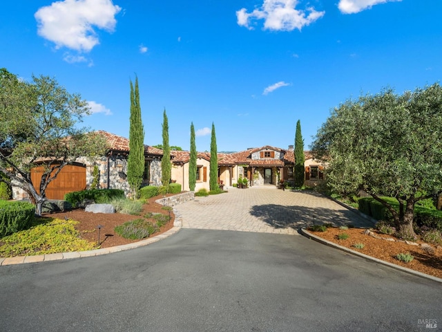 mediterranean / spanish home featuring a tiled roof, stone siding, decorative driveway, and stucco siding