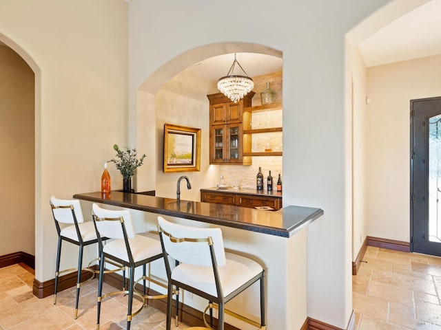 bar featuring stone tile flooring, baseboards, decorative backsplash, and indoor wet bar