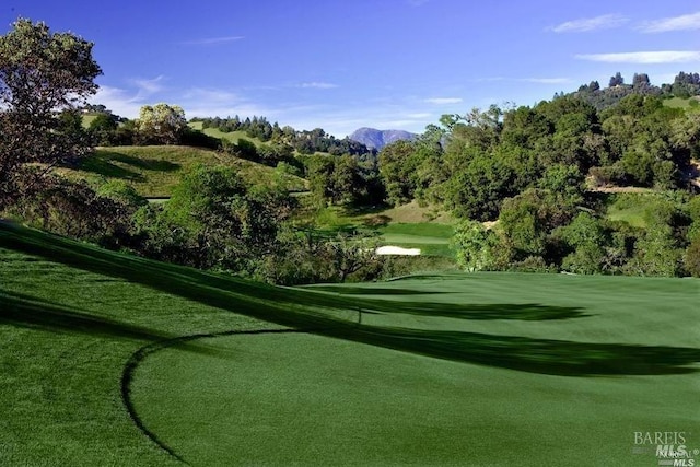 view of home's community with a mountain view, view of golf course, and a lawn
