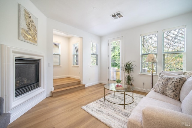 living area featuring baseboards, visible vents, a glass covered fireplace, and light wood-style floors