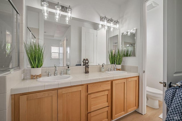 full bathroom with a sink, toilet, double vanity, and wood finished floors