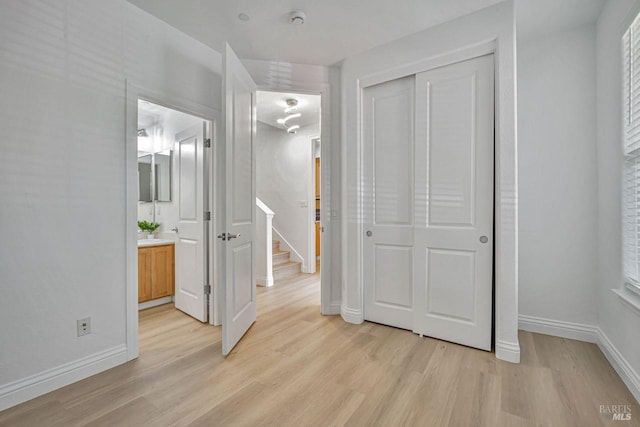 unfurnished bedroom featuring light wood-style floors, a closet, baseboards, and ensuite bath