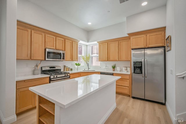 kitchen featuring light wood-style flooring, light countertops, a kitchen island, appliances with stainless steel finishes, and a sink