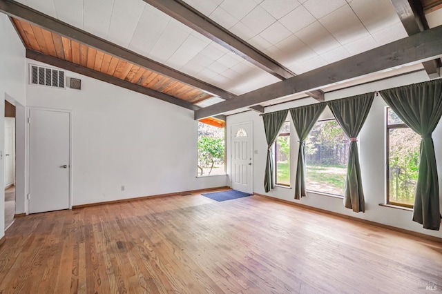 empty room featuring baseboards, lofted ceiling with beams, wood-type flooring, and visible vents