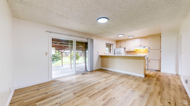 kitchen with white appliances, light wood-style flooring, a peninsula, a textured ceiling, and light countertops
