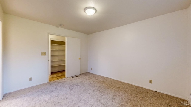 unfurnished bedroom featuring a walk in closet, a closet, baseboards, and carpet