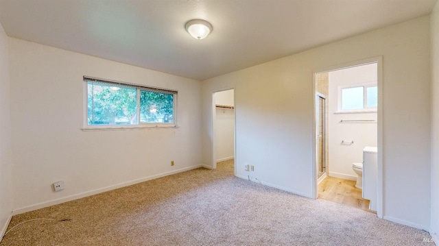 unfurnished bedroom featuring a closet, baseboards, a walk in closet, connected bathroom, and light colored carpet