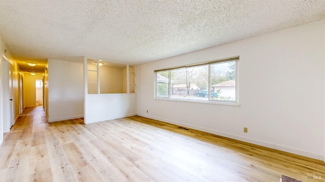 empty room with a textured ceiling, wood finished floors, baseboards, and visible vents