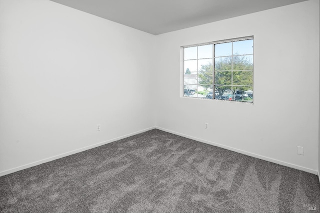 unfurnished room featuring baseboards and dark colored carpet