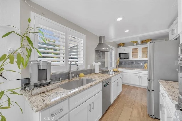 kitchen with wall chimney range hood, white cabinetry, black appliances, decorative backsplash, and a sink