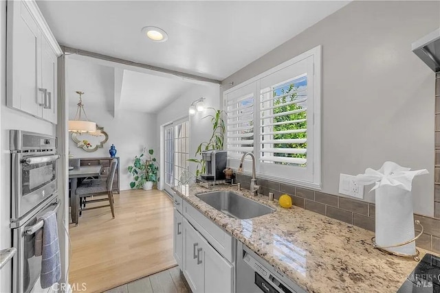kitchen with light wood-type flooring, stainless steel double oven, a sink, and white cabinetry